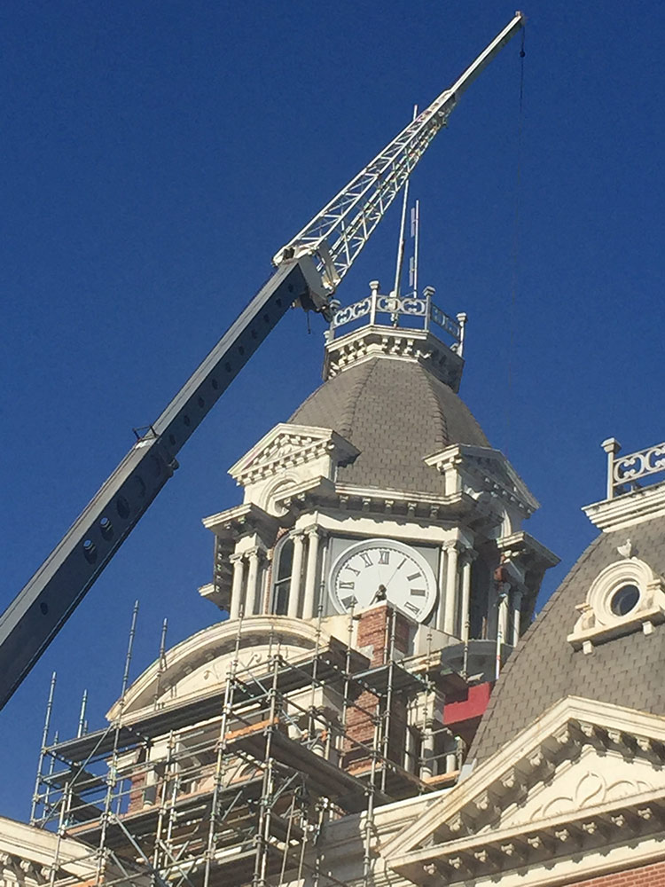 crane boom near the clock at the top of a courthouse